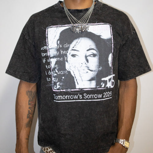 A man wearing a faded black graphic t-shirt with a portrait of Sade and the text 'Tomorrow's Sorrow 2026', paired with a camouflage baseball cap that reads 'GOD'S FAVORITE'.